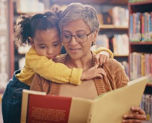 grandma with grandchild in library, hug and bond while reading together. Education, storytelling and grandma teaching girl, relax and enjoy books, story and child development